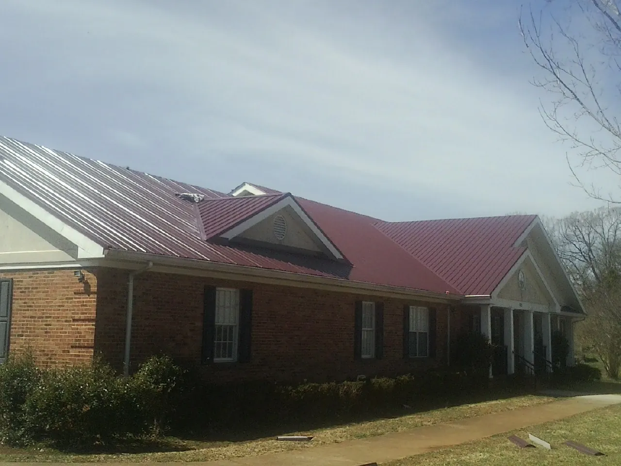 Red metal roof with gabled entries on a long brick building, from a Hail Damage Roof Repair job in Meridian