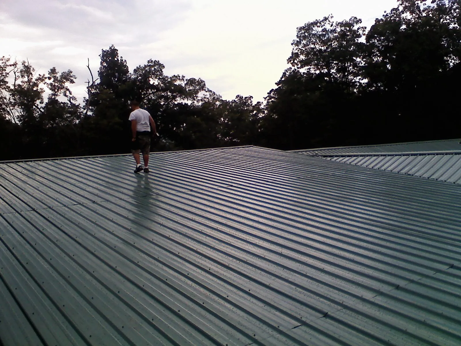 Roofer walking a wide expanse of new green metal roofing in Meridian